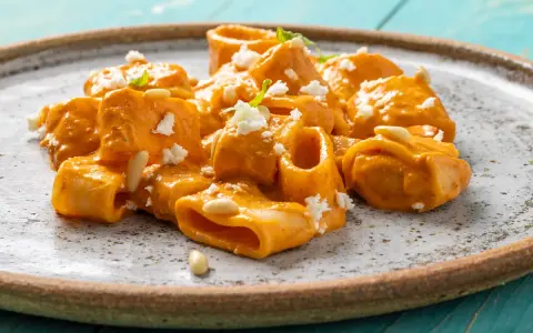 Paccheri cremosi con salsa arancione, formaggio sbriciolato e pinoli. Un piatto che ricorda il sapore del brodo vegetale Bimby.