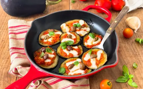 Melanzane in padella con pomodoro e mozzarella, guarnite con olive e basilico. Un antipasto invitante e saporito.