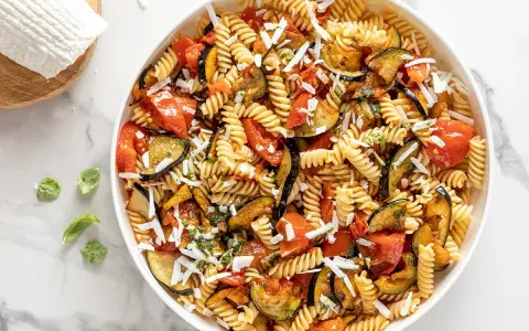 Un piatto invitante di pasta fredda alla norma con melanzane, pomodori e ricotta salata grattugiata.