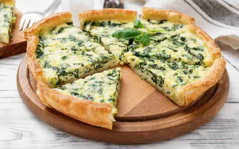Una fetta di torta rustica ricotta e spinaci, con crosta dorata e ripieno cremoso, guarnita con basilico fresco.