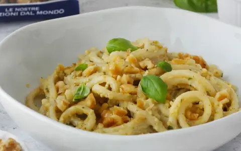 Pasta condita con un cremoso pesto di noci, guarnita con basilico fresco e noci croccanti.