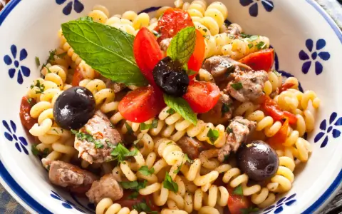 Fusilli con pesce spada, pomodorini, olive nere e menta fresca in una ciotola decorata.