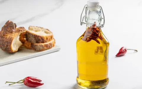 Olio al peperoncino in bottiglia, con pane rustico e peperoncini rossi. Un tocco piccante per ogni piatto.