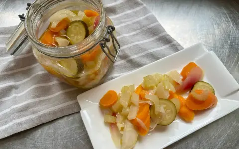 Giardiniera fatta in casa: carote, sedano, cipolle e cetrioli sottaceto in un barattolo e su un piatto. Ricetta facile e gustosa.