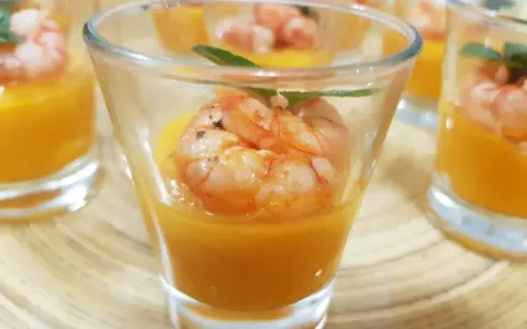 Deliziosi finger food gamberi su crema arancione in bicchierini, guarniti con menta.