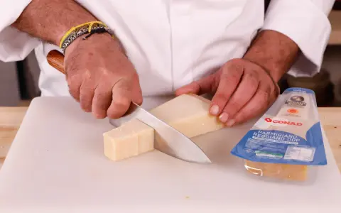 Mani che tagliano un pezzo di Parmigiano Reggiano, pronto per una deliziosa fonduta.