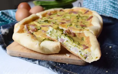 Torta salata con zucchine e pancetta, una fetta tagliata mostra il ripieno gustoso. Ingredienti freschi e profumati.