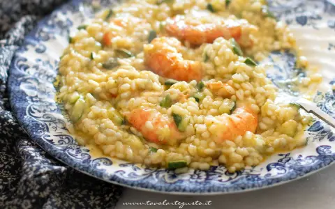 Un cremoso risotto zucchine e gamberetti, servito su un piatto decorato.