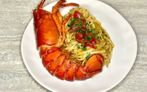 Un piatto di linguine all'astice, con pasta condita e astice intero, guarnito con pomodorini e prezzemolo.