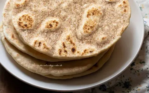 Piatto di piadine senza strutto, dorate e leggermente maculate, impilate su un piatto bianco.