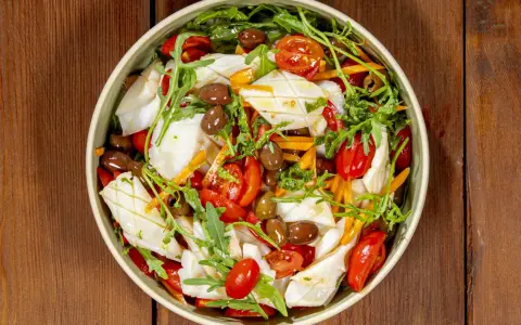 Insalata di calamari fresca con pomodorini, olive, rucola e carote julienne, un piatto leggero e saporito.