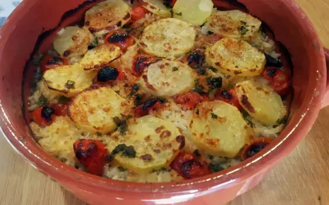 Piatto di riso patate e cozze cotto al forno, con pomodorini e erbe aromatiche, servito in una terrina di terracotta.