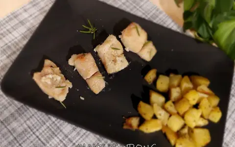 Pezzi di baccalà al forno con rosmarino e patate arrosto su piatto nero.