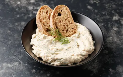 Mousse di tonno cremosa con erbe aromatiche, guarnita con aneto e servita con fette di pane integrale tostato.