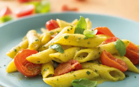 Penne al pesto con pomodorini freschi e basilico, un piatto colorato e saporito.