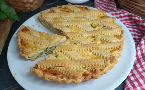 Una deliziosa crostata salata con zucchine e formaggio, con una griglia di pasta dorata e un pezzo tagliato.