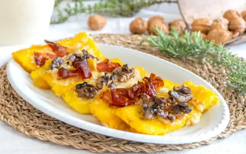 Deliziosi crostini di polenta freddi con prosciutto croccante e noci, un antipasto rustico e saporito.