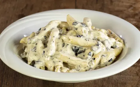 Penne cremose con pezzetti scuri, un piatto invitante di pasta alla cenere, servito in una ciotola bianca su un tavolo di legno rustico.