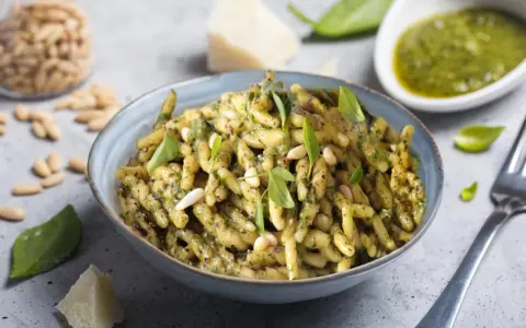 Un piatto di trofie al pesto, condite con basilico fresco, pinoli e parmigiano. Una ricetta classica e gustosa.