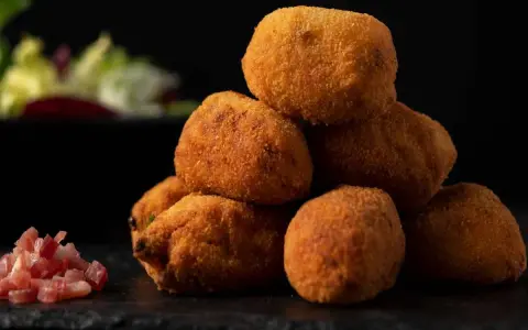 Pile di supplì alla carbonara dorati e croccanti, con guanciale a cubetti e insalata sfocata sullo sfondo.