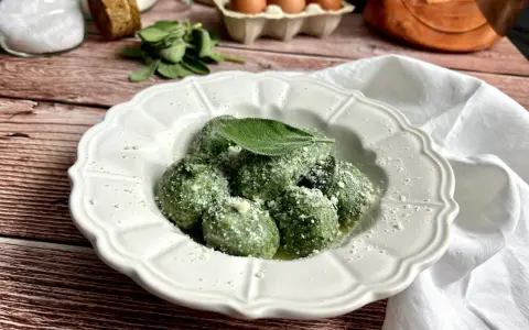 Gnudi verdi, una deliziosa ricetta con spinaci e ricotta, guarniti con parmigiano e una foglia di salvia.