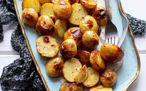 Patate novelle al forno dorate e croccanti, servite su un piatto azzurro con forchetta.