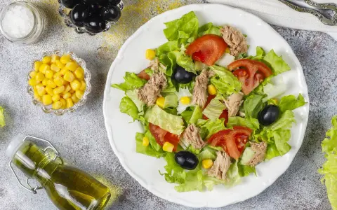 Deliziosa insalata di tonno con lattuga croccante, pomodoro, mais e olive nere. Un piatto fresco e leggero, perfetto per ogni occasione.
