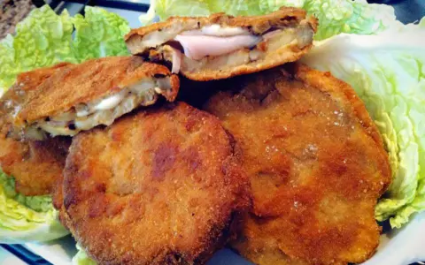 Cordon bleu di melanzane impanati e fritti, ripieni di prosciutto e formaggio filante, serviti su un letto di lattuga croccante.