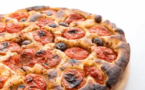 Focaccia barese dorata e fragrante, con pomodorini succosi e olive nere, pronta per essere gustata.