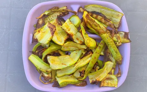 Piatto rosa pieno di zucchine grigliate, tagliate a listarelle e leggermente abbrustolite, pronte per essere gustate.