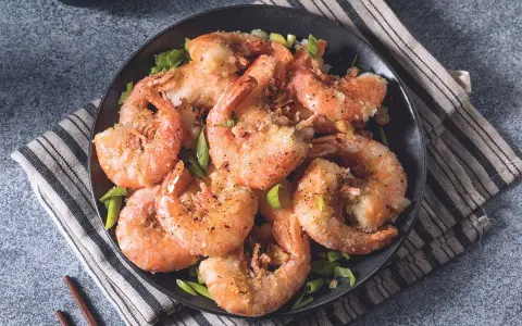 Gamberi sale e pepe croccanti, dorati e profumati, serviti su un piatto scuro con erba cipollina fresca.