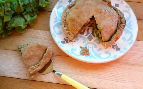 Torta salata con scarola, acciughe e mozzarella, appena sfornata, con una fetta servita su un piatto decorato.