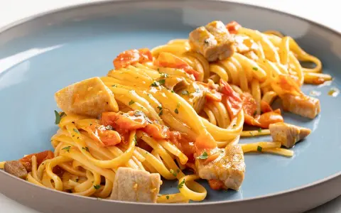 Un piatto invitante di pasta con tonno fresco, pomodorini e prezzemolo, condito con una salsa dorata.