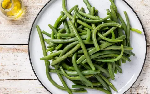 Un piatto di fagiolini lessi, freschi e verdi, pronti per essere gustati. Accanto, un piccolo recipiente con olio d'oliva.