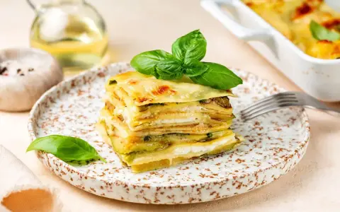 Una fetta di parmigiana di zucchine, stratificata e dorata, guarnita con basilico fresco.