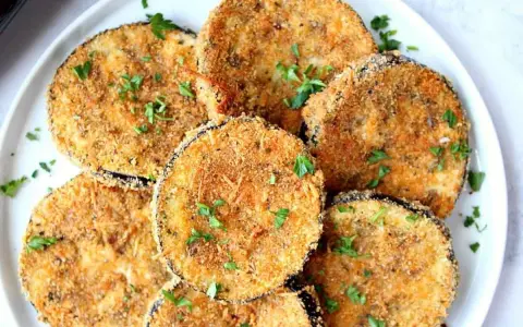 Fette dorate di melanzane impanate al forno, guarnite con prezzemolo fresco. Un antipasto croccante e saporito.
