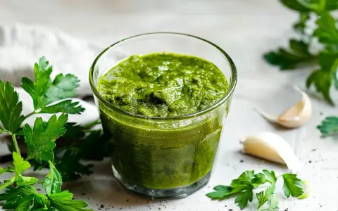 Un bicchiere di vibrante salsa verde, con prezzemolo fresco e spicchi d'aglio sullo sfondo.