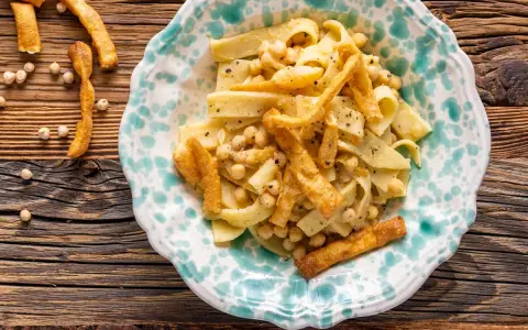 Piatto di ciceri e tria, pasta fresca con ceci e croccanti sfoglie fritte, servito in un piatto decorato.