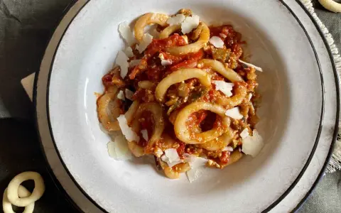 Un piatto di anellini alla pecorara, pasta a forma di anello condita con sugo di pomodoro, verdure e scaglie di formaggio.