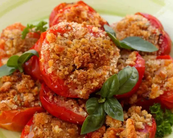 Pomodori al forno ripieni di pangrattato e erbe aromatiche, guarniti con basilico fresco.
