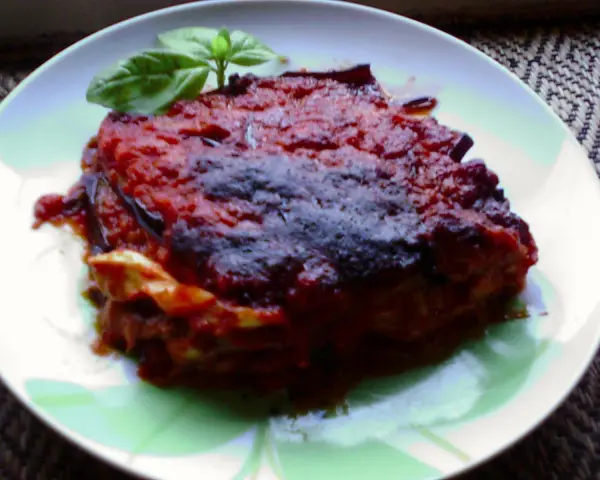 Una porzione di parmigiana di melanzane napoletana, ricca e saporita, guarnita con basilico fresco.