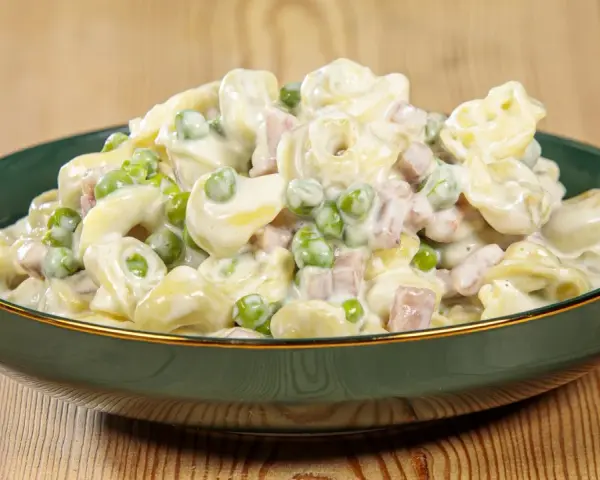 Un piatto invitante di tortellini panna e prosciutto, con piselli verdi, conditi con una cremosa salsa bianca.