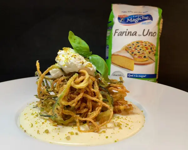 Deliziosi spaghetti di zucchine fritte croccanti, serviti su una crema vellutata e guarniti con ricotta fresca e basilico.