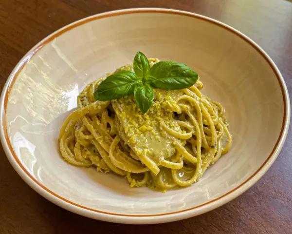 Spaghetti conditi con un cremoso pesto di limone, guarniti con basilico fresco. Una deliziosa ricetta per un primo piatto estivo.