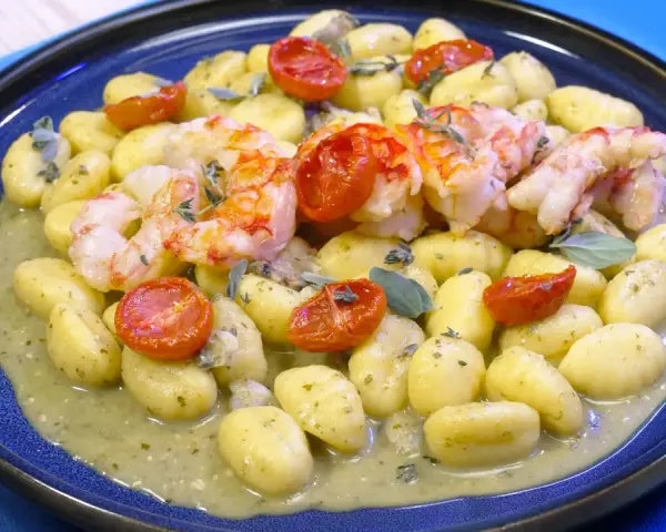 Gnocchi con pesto, gamberi succulenti e pomodorini confit. Un piatto che celebra i sapori del mare e della terra.