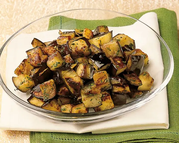 Melanzane a funghetto ricetta della nonna: cubetti dorati e saporiti, conditi con erbe aromatiche, in una ciotola di vetro.