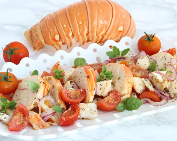 Aragosta alla catalana, un piatto fresco con aragosta, pomodorini, cipolla rossa e basilico, servito su un vassoio bianco.