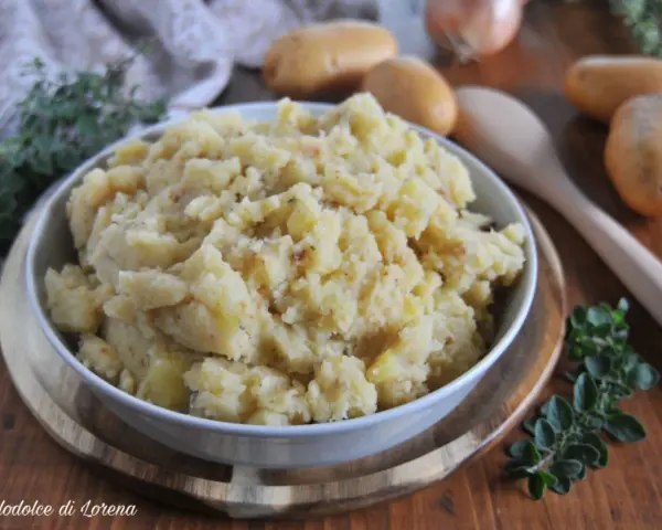 Un saporito piatto di patate in tecia, cotte con erbe aromatiche e spezie, servite in una ciotola su un tagliere di legno.