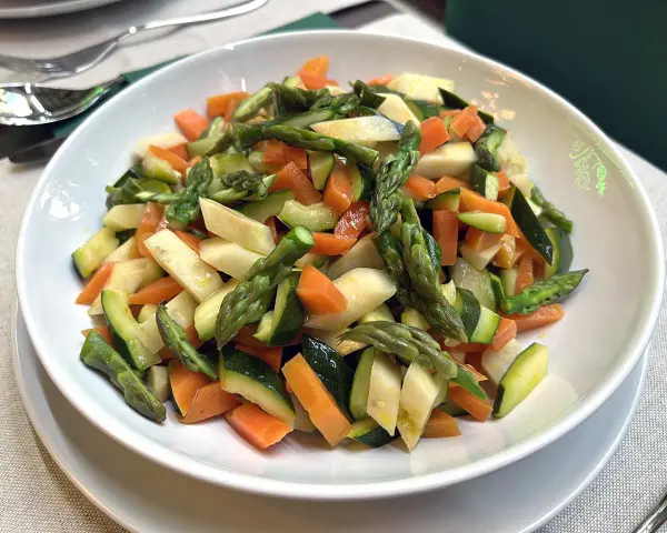 Un piatto invitante di verdure in padella: asparagi, carote e zucchine tagliate a pezzetti, condite con un filo d'olio.