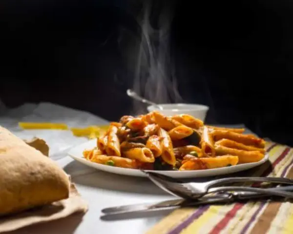 Piatto fumante di penne alla vodka, con pane croccante e posate pronte per gustare questo classico italiano.
